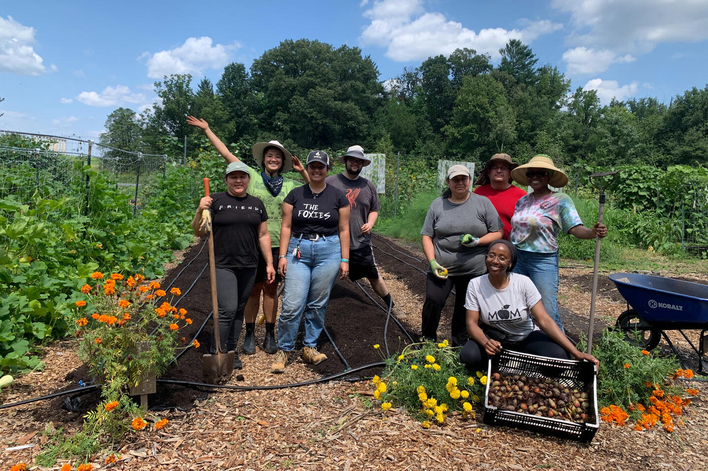 Photo of a group of people wearing sun hats and holding gardening tools smiling for the camera during a garden work day